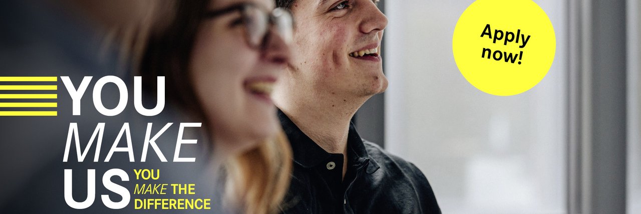 Two young employees during a conversation – The slogan "You make us. You make the difference" can be seen on the left-hand side, accompanied by a yellow button with "Apply now!"