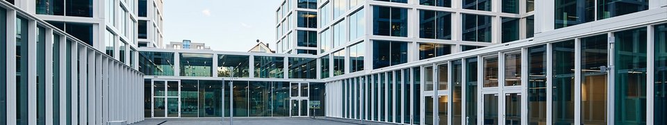 Gebäudeansicht des Daimler Truck Hauptsitzes in Leinfelden mit großen Glasfassaden und im Vordergrund das Firmenlogo im Innenhof.