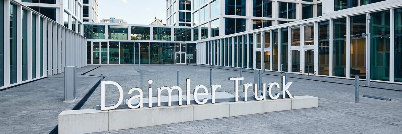 Gebäudeansicht des Daimler Truck Hauptsitzes in Leinfelden mit großen Glasfassaden und im Vordergrund das Firmenlogo im Innenhof.