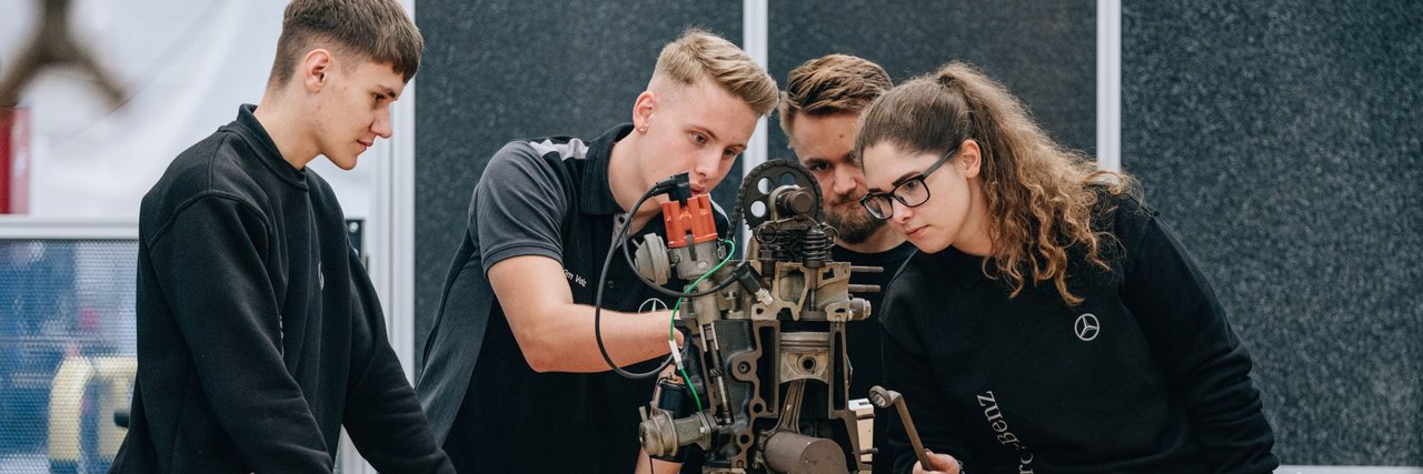 A group of young team members analyse a mechanical device in a workshop.