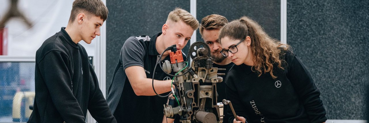 Eine Gruppe von jungen Teammitgliedern analysiert eine mechanische Vorrichtung in einer Werkstatt.