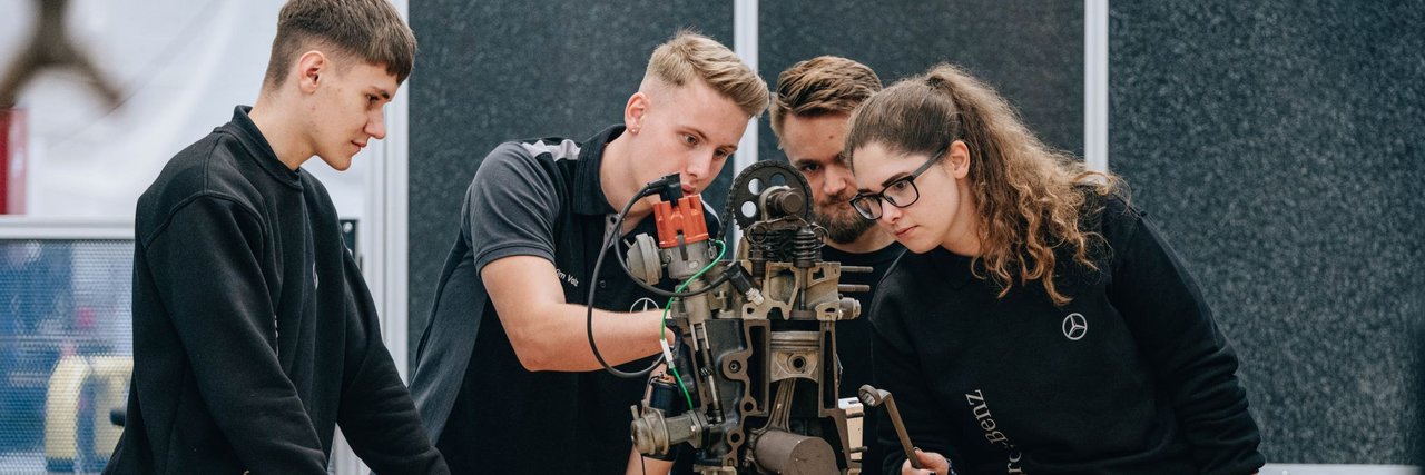 Eine Gruppe von jungen Teammitgliedern analysiert eine mechanische Vorrichtung in einer Werkstatt.