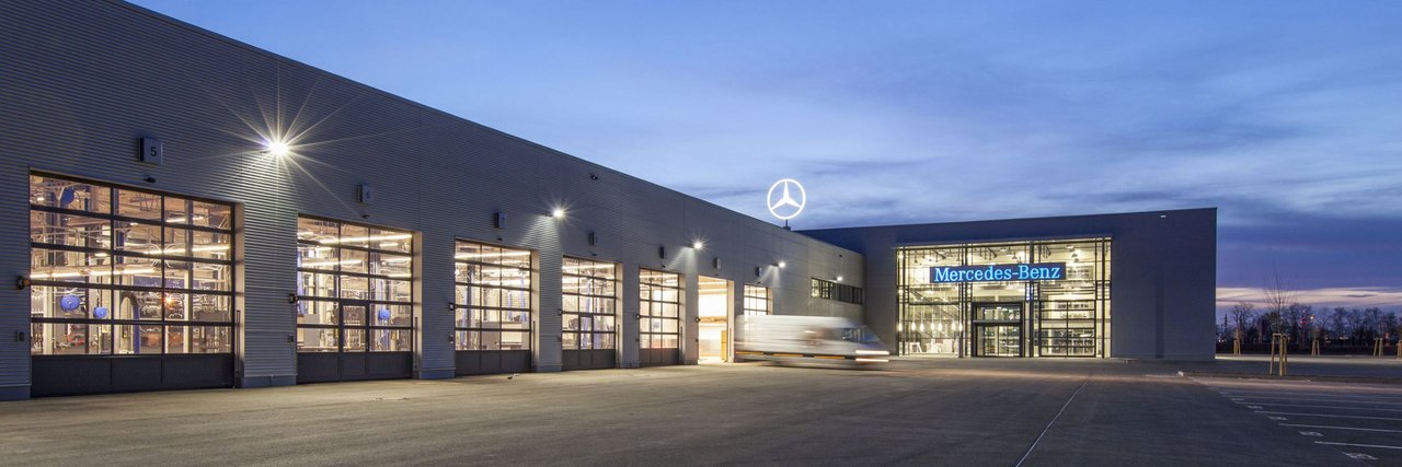 Das Mercedes-Benz Nutzfahrzeugzentrum Mannheim bei Dämmerung mit beleuchteter Glasfassade und Servicehalle.