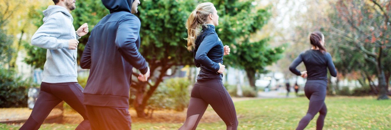 Four people are jogging together through a park. This image represents the sports and health programs at Daimler Truck that promote exercise and balance to the working day.