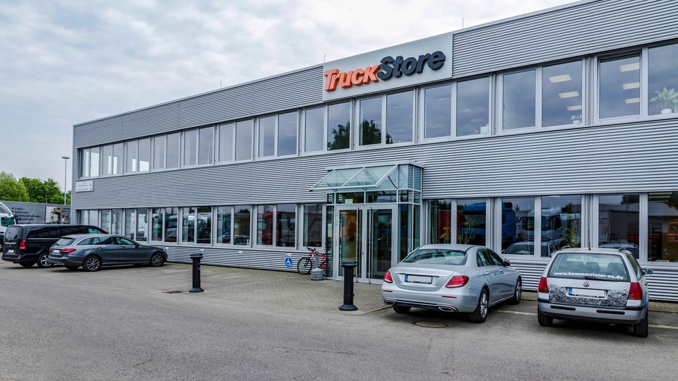 Exterior view of a TruckStore building in Köngen with glass entrance and parked cars in the foreground.