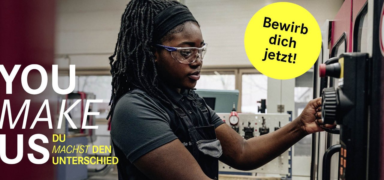 Eine Mitarbeiterin in Arbeitskleidung und mit Schutzbrille bedient konzentriert eine CNC-Maschine in einer Werkshalle, mit dem Slogan „YOU MAKE US – YOU MAKE THE DIFFERENCE“ und einem „Bewirb dich jetzt!“-Button.