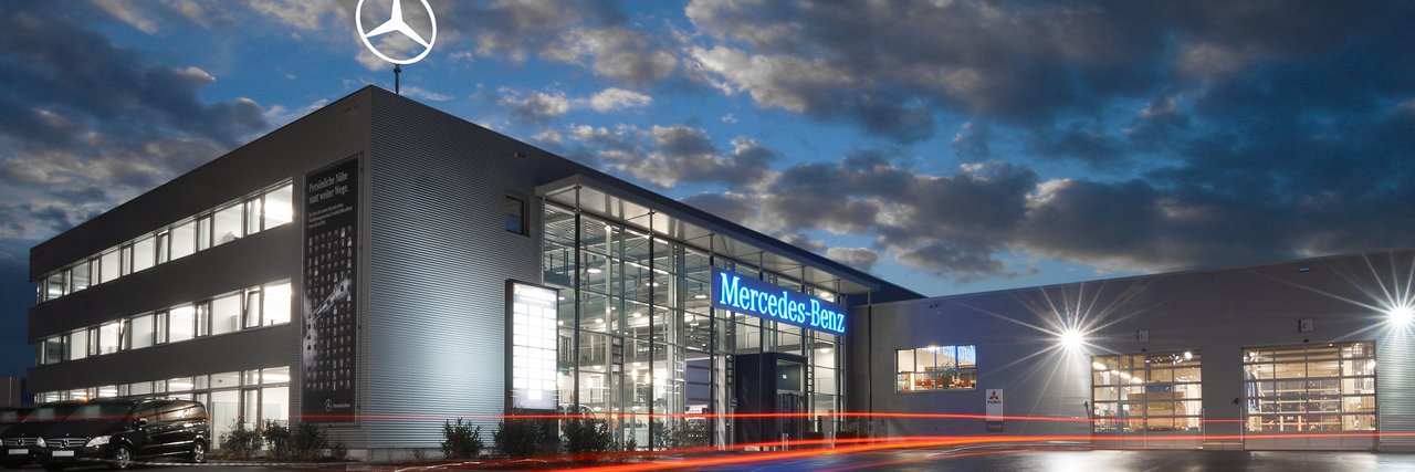 Abendaufnahme des Mercedes-Benz Nutzfahrzeugzentrums Frankfurt, mit modernen Glasfronten und geparkten Nutzfahrzeugen.