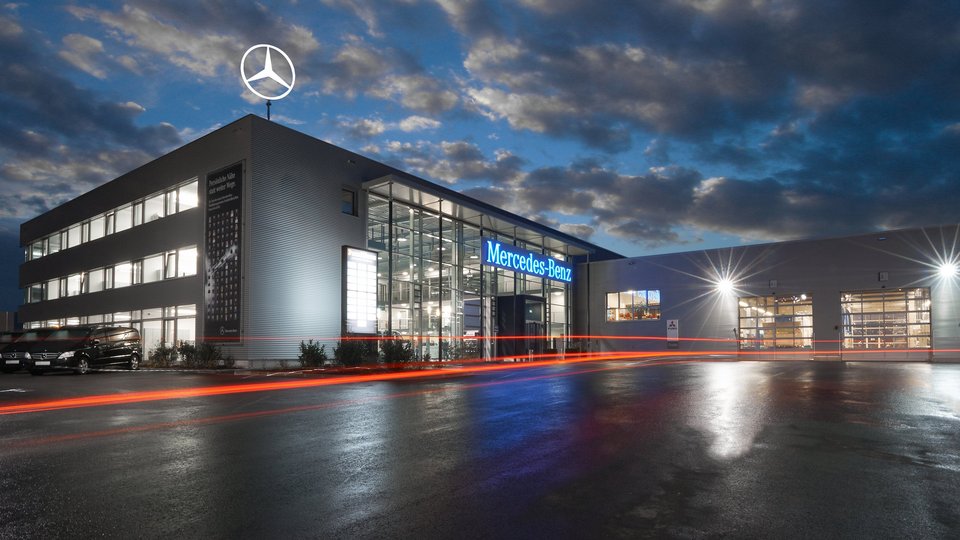 Abendaufnahme des Mercedes-Benz Nutzfahrzeugzentrums Frankfurt, mit modernen Glasfronten und geparkten Nutzfahrzeugen.