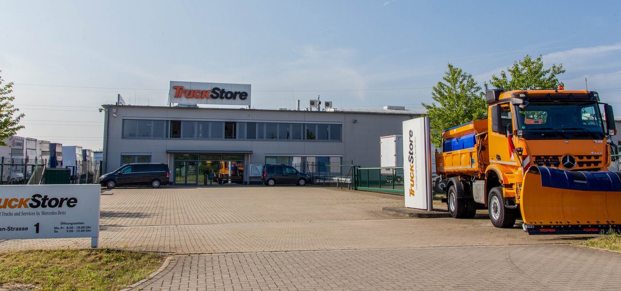 Entrance area of the TruckStore Recklinghausen with a large orange Mercedes-Benz winter service vehicle.