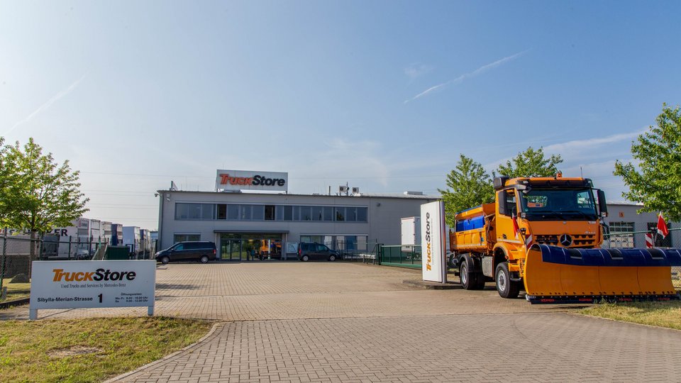 Entrance area of the TruckStore Recklinghausen with a large orange Mercedes-Benz winter service vehicle.