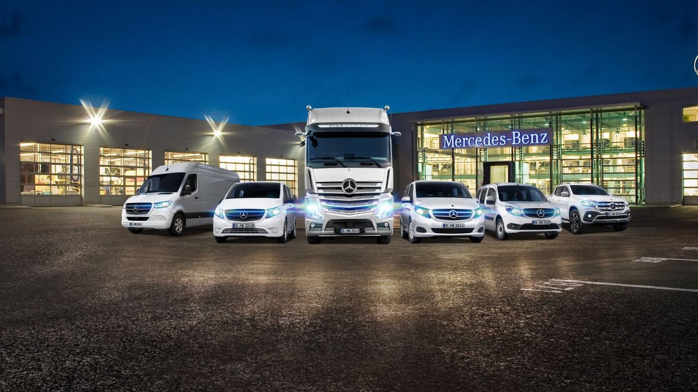 Außenansicht eines beleuchteten Daimler Truck Nutzfahrzeugzentrums mit mehreren ausgestellten Mercedes-Benz Fahrzeugen.