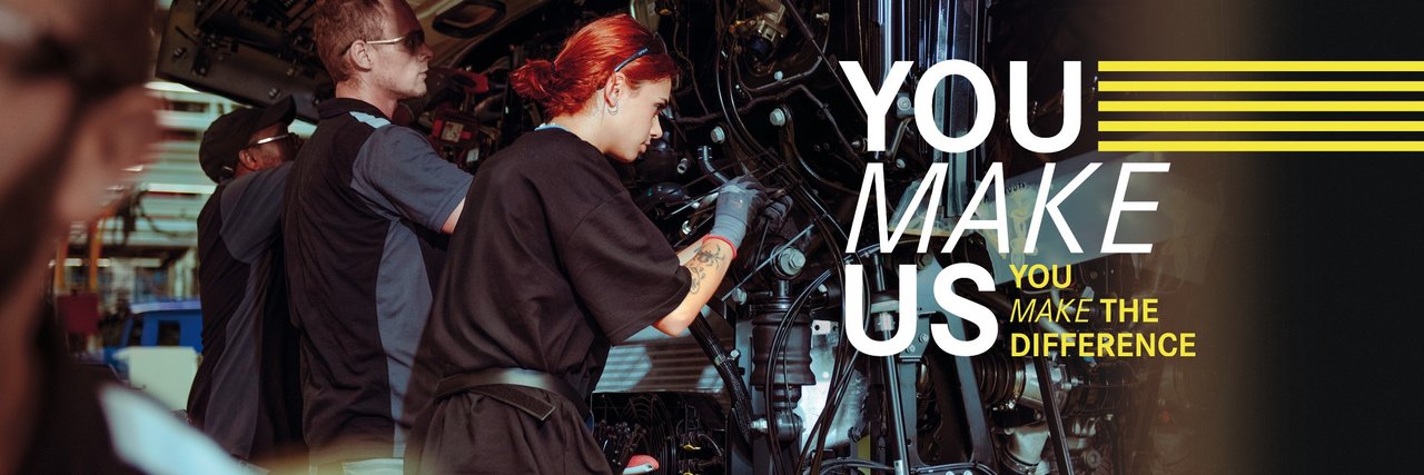 Junge Mitarbeitende montieren Teile an einem Lkw in der Daimler Truck Produktion – Teamarbeit und Einsatz im Ferienjob. Text im Bild: "You make us – You make the difference."