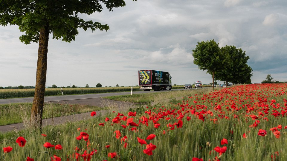 Der eActros 600 fährt rückwärts über öffentliche Straßen, im Vordergrund ist ein Mohnfeld zu sehen.