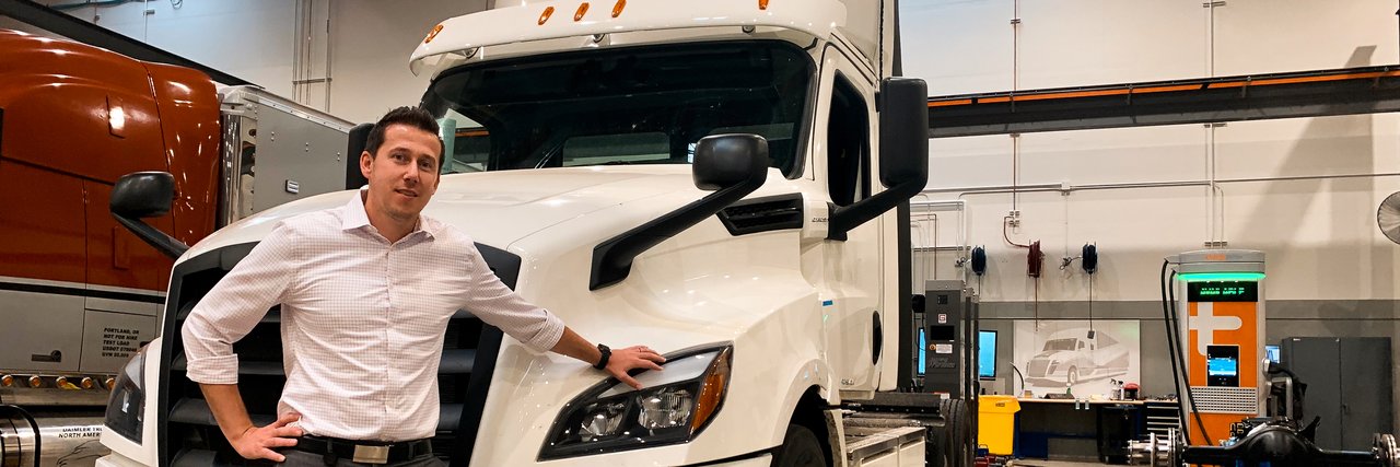 Alexander Voets leans against a white Freightliner eCascadia in a factory hall.