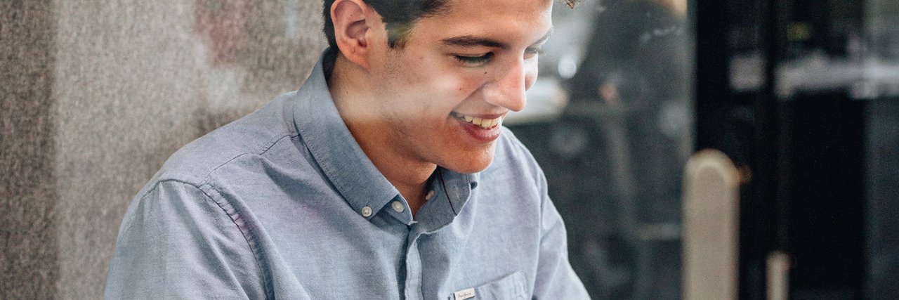 A young commercial trainee smiles as he works on his laptop in a glazed meeting room.