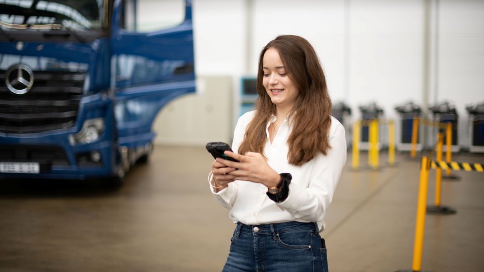 Eine Mitarbeiterin arbeitet am Handy, im Hintergrund sieht man einen Truck.