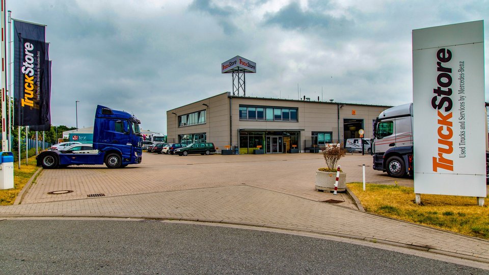 TruckStore building in Bremen with flags, a blue and a silver truck in the foreground.