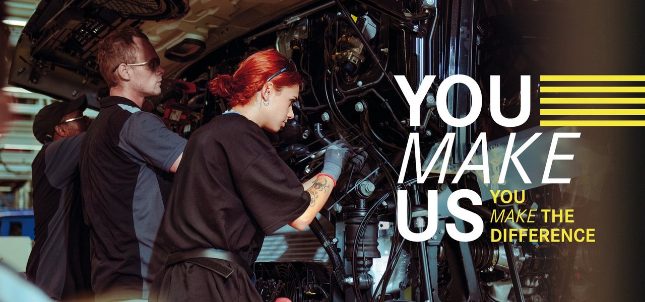 Employees work on the production of a truck, supported by the Daimler Truck campaign slogan "YOU MAKE US - YOU MAKE THE DIFFERENCE".