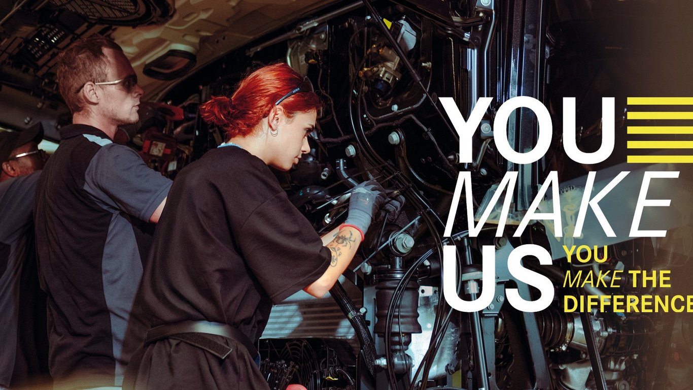 Mitarbeitende arbeiten an der Fertigung eines Lkw, unterstützt durch den Daimler Truck Kampagnenslogan „YOU MAKE US – YOU MAKE THE DIFFERENCE“.
