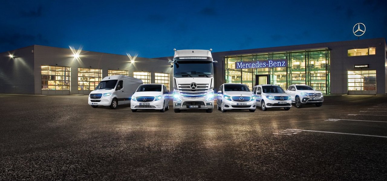 Außenansicht eines beleuchteten Daimler Truck Nutzfahrzeugzentrums mit mehreren ausgestellten Mercedes-Benz Fahrzeugen.
