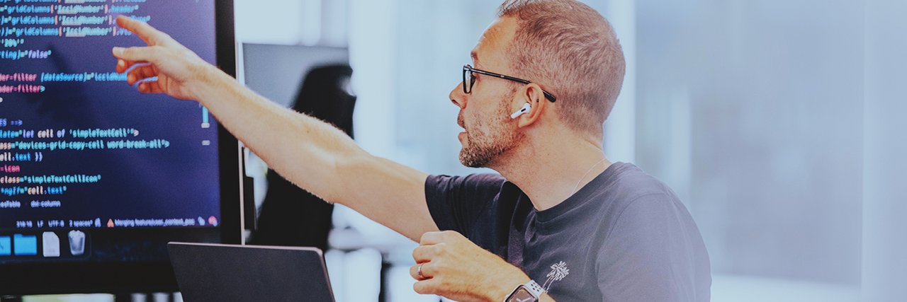 A software developer points to a code on a screen during a meeting.