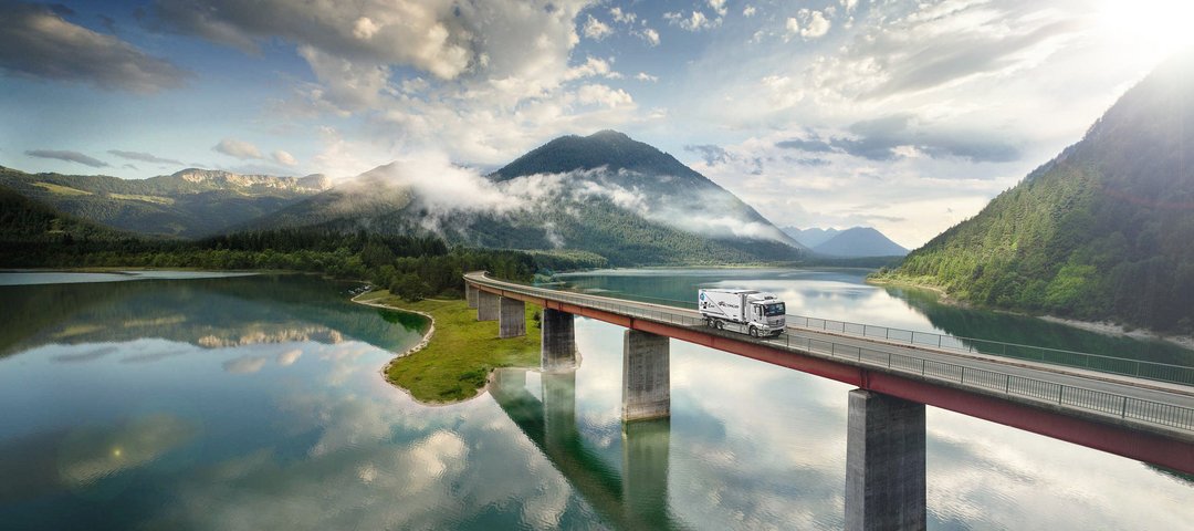 Mercedes-Benz eActros fährt über eine Brücke über einem See in den Bergen