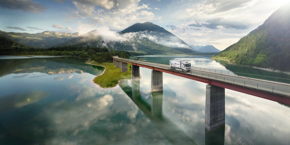 Mercedes-Benz eActros fährt über eine Brücke über einem See in den Bergen