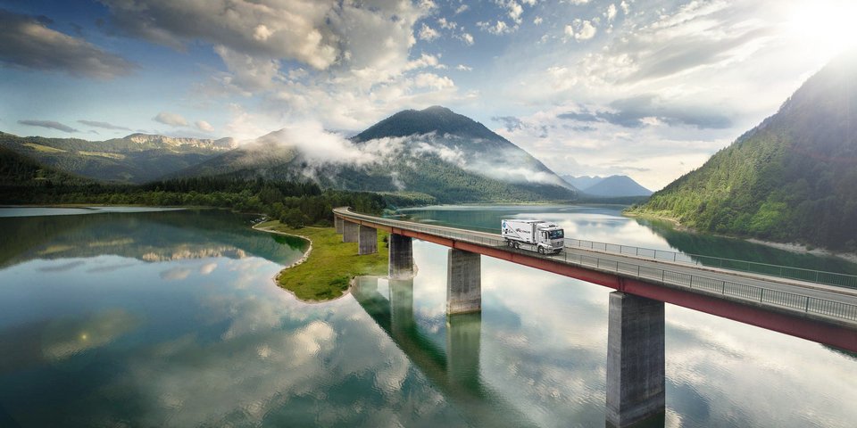 Mercedes-Benz eActros fährt über eine Brücke über einem See in den Bergen