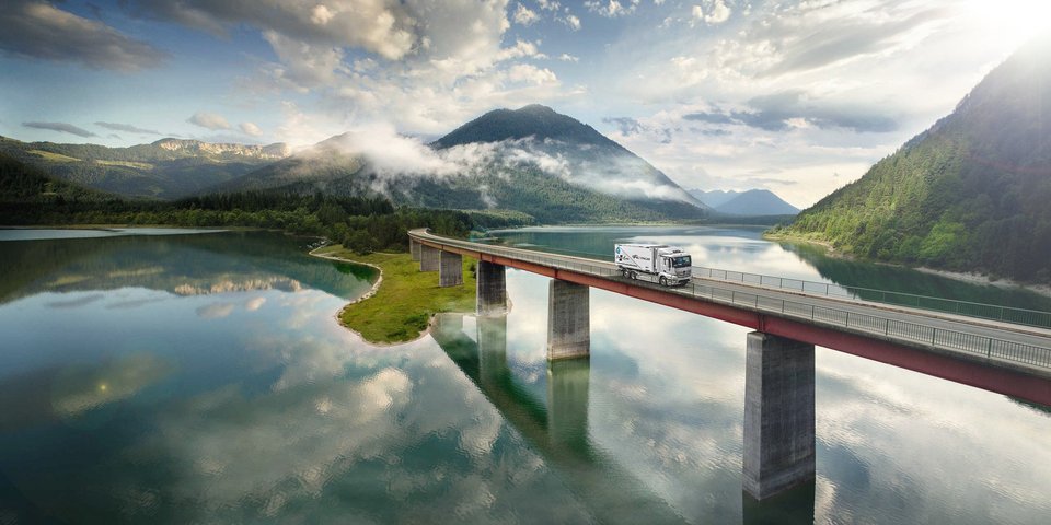Mercedes-Benz eActros drives over a bridge over a lake in the mountains