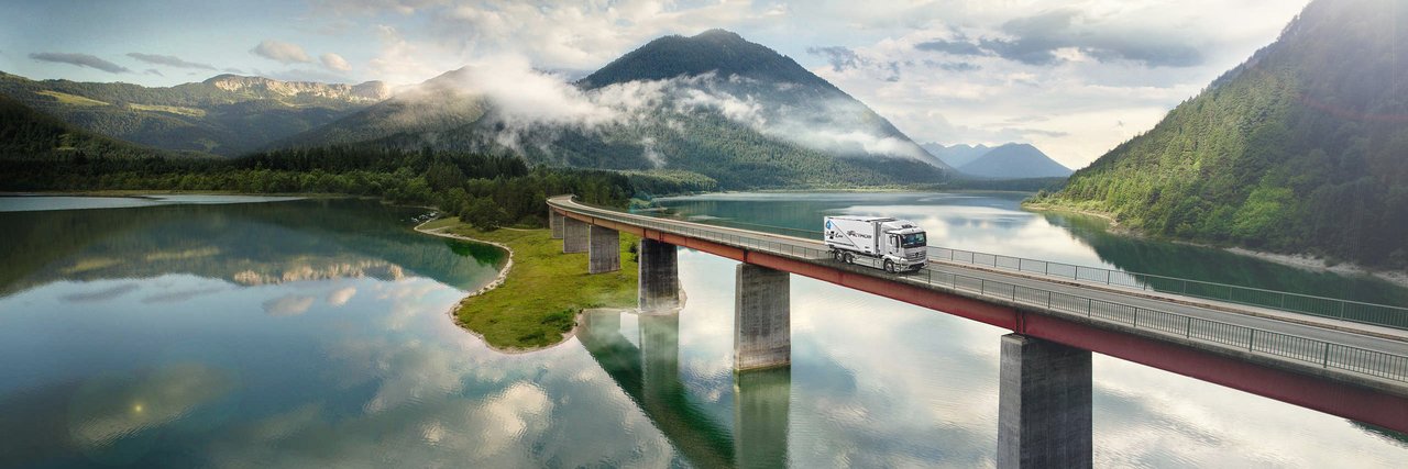 Mercedes-Benz eActros fährt über eine Brücke über einem See in den Bergen