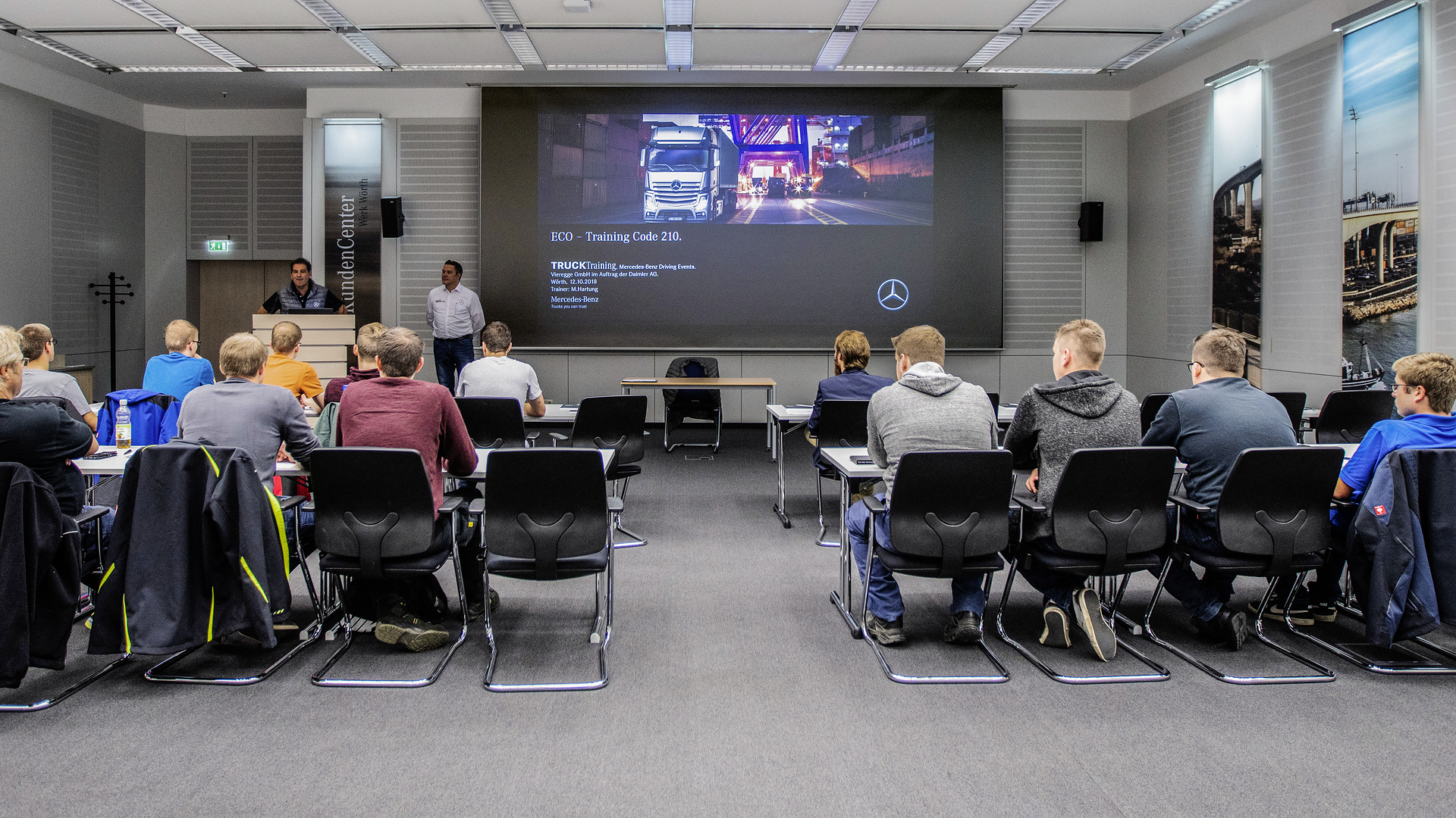 Martin Gairing (links am Pult), Leitung TruckTraining Mercedes-Benz Lkw in Wörth, begrüßt di e Teilnehmer des BEST-BKF-Wettbewerbs und stellt Marcus Hartung (rechts), Trainer des Eco Trainings, vor. BEST-BKF – Gewinnertag im Mercedes-Benz Lkw-Werk Wörth: Die junge Trucker-Generation übernimmt das Steuerrad