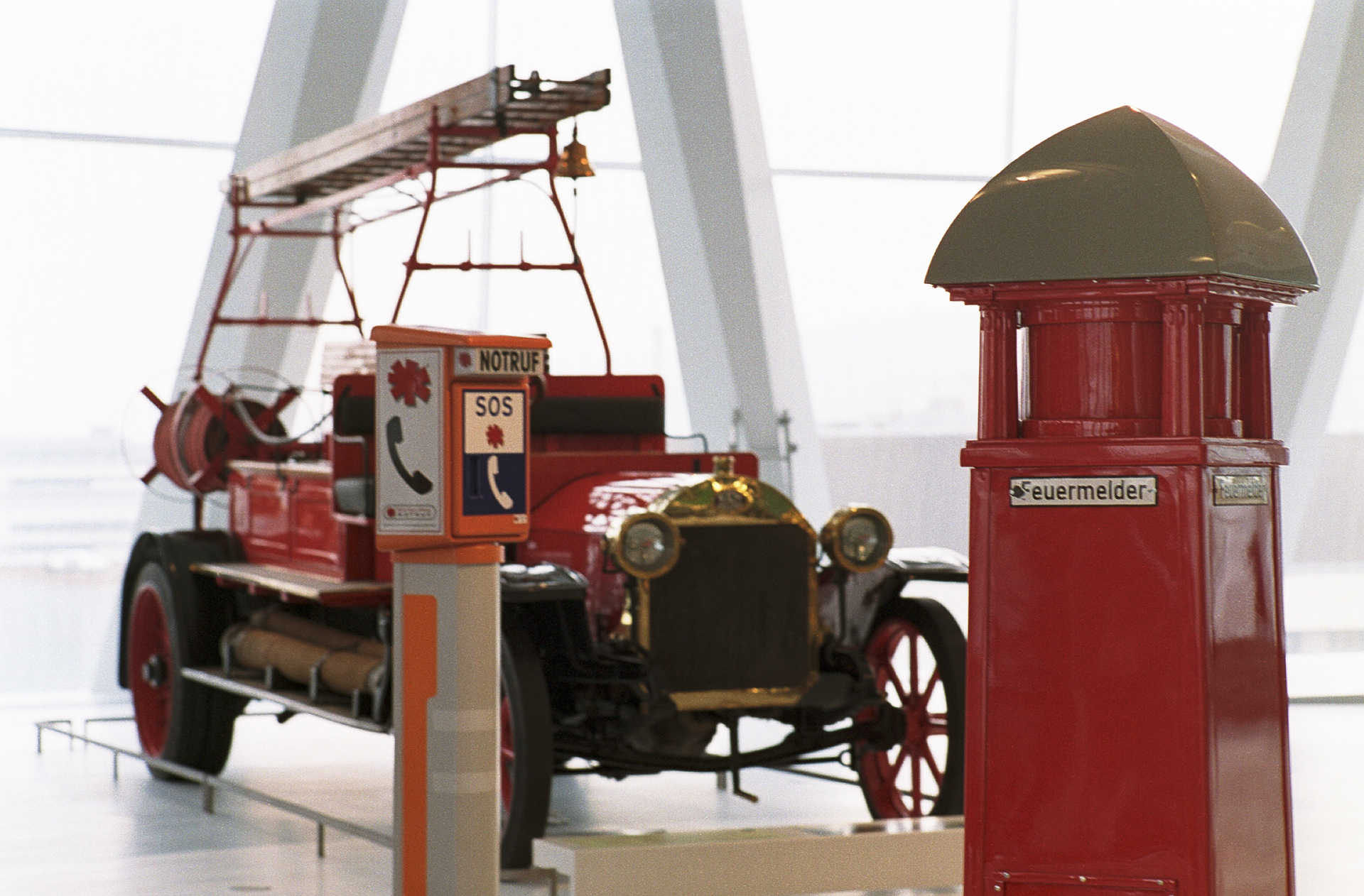 Mercedes-Benz Museum, Raum Collection 3: Galerie der Helfer. Historischer Feuermelder (rechts), im Hintergrund eine Benz Feuerwehr-Motorspritze von 1912. (Fotosignatur der Mercedes-Benz Classic Archive: D121366) Welcher Daimler-Motor ist so stark wie 32 Feuerwehrleute?
