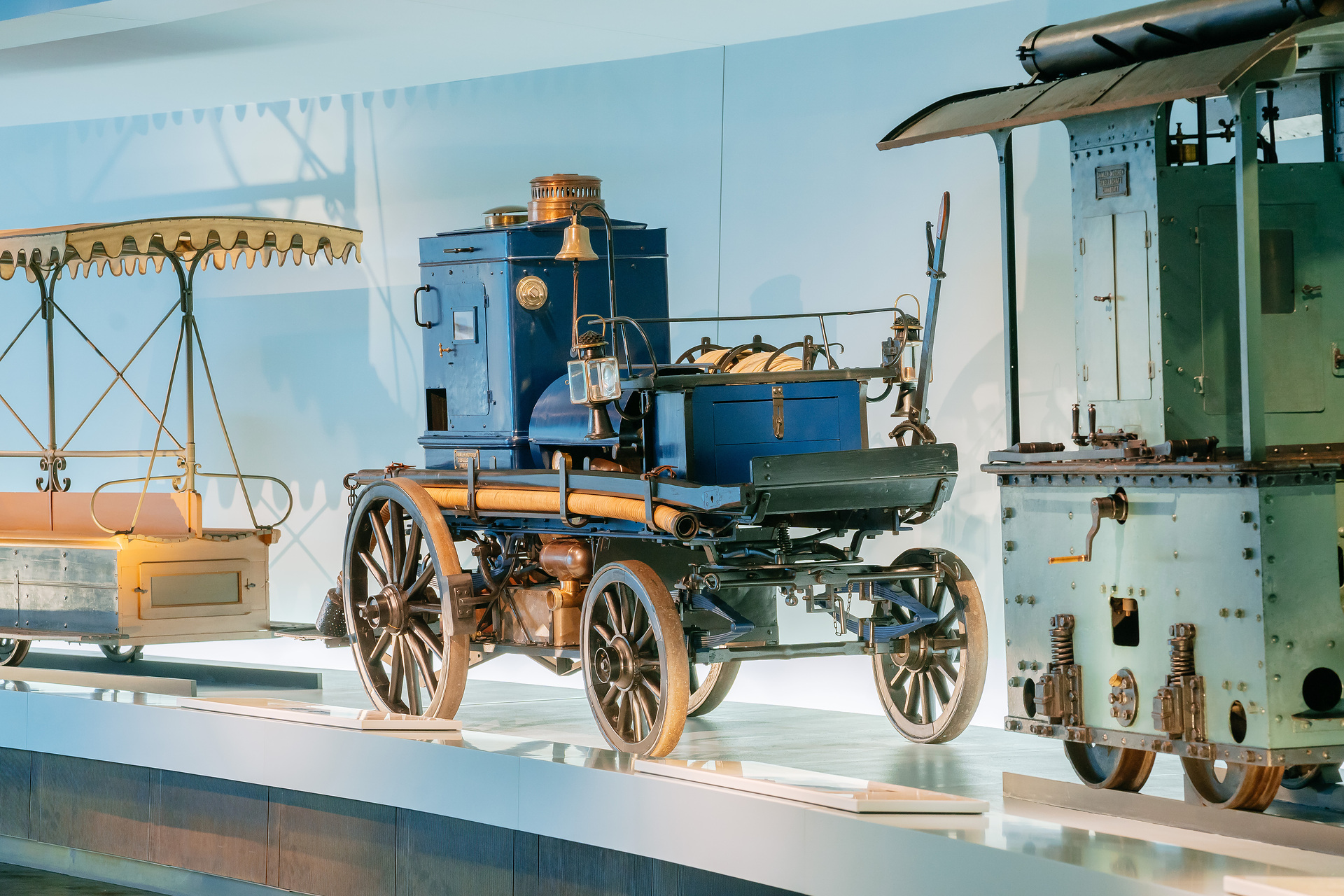 Mercedes-Benz Museum, Raum Mythos 1: Pioniere – Die Erfindung des Automobils, 1886 bis 1900. Daimler Motor-Feuerspritze aus dem Jahr 1892 mit 3-Liter-Zweizylindermotor (5,1 kW/7 PS) als Pumpenantrieb und zur Bespannung mit Pferden. Gesamtansicht von rechts vorn zwischen den Schienenfahrzeugen Daimler Motor-Waggonet von 1891 (links) und Daimler Motor-Lokomotive von 1893 (rechts). Welcher Daimler-Motor ist so stark wie 32 Feuerwehrleute?