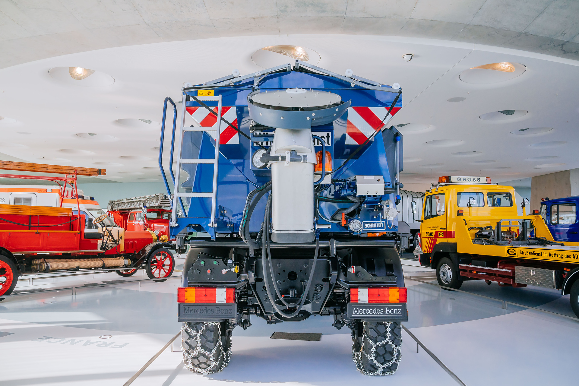 Mercedes-Benz Museum, Collection Room 3: The Gallery of Helpers. Mercedes-Benz Unimog U 500 of the 405 model series, winter service vehicle with snow blower, snow chains and gritting body from 2004. General view from the rear with the spreading disc for road salt folded up. The universal solution against snow and icy roads: The Unimog U 500 with winter maintenance equipment