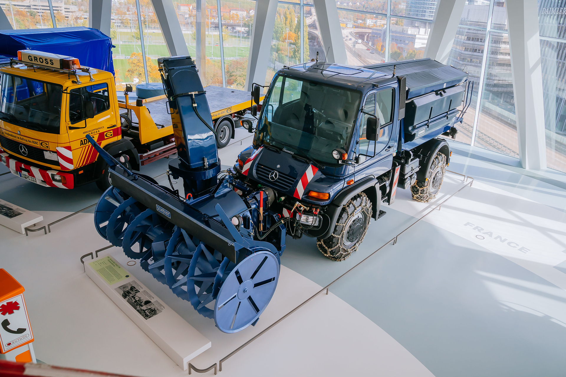 Mercedes-Benz Museum, Collection Room 3: The Gallery of Helpers. Mercedes-Benz Unimog U 500 of the 405 model series, winter service vehicle with snow blower, snow chains and gritting body from 2004. General view from an elevated perspective from the front left. The universal solution against snow and icy roads: The Unimog U 500 with winter maintenance equipment