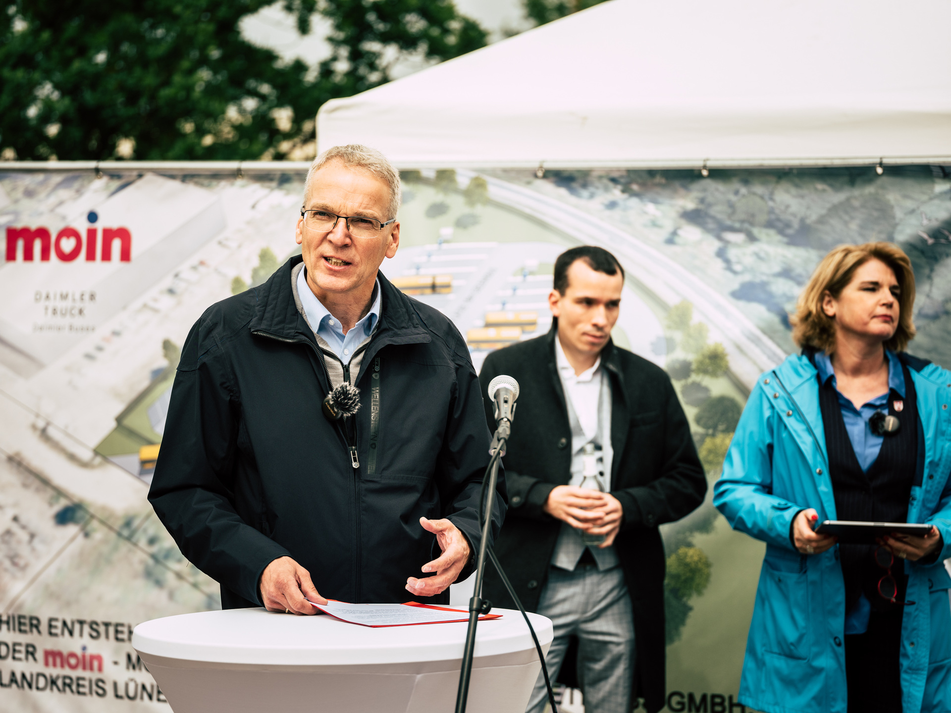 Daimler Buses Solutions, Spatenstich für neues Busdepot in Lüneburg für MOIN Gmbh, Jens Böther (Landrat von Lüneburg) am Rednerpult, im Hintergrund: Nikolas Wenzel (Geschäftsführer MOIN GmbH) und Claudia Kalisch (Oberbürgermeisterin von Lüneburg) Premiere mit MOIN in Lüneburg: Daimler Buses errichtet erstmals komplett neuen E-Bus Betriebshof eines Kunden