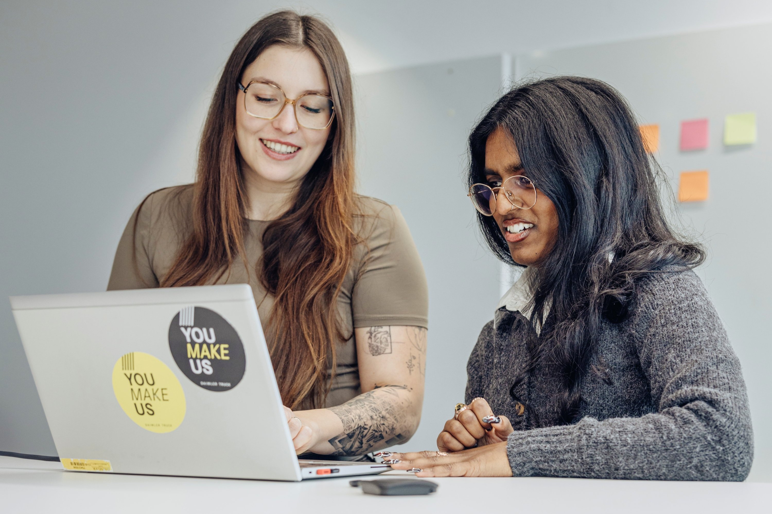 Zwei Mitarbeiterinnen schauen gemeinsam auf den Laptop-Bildschirm.