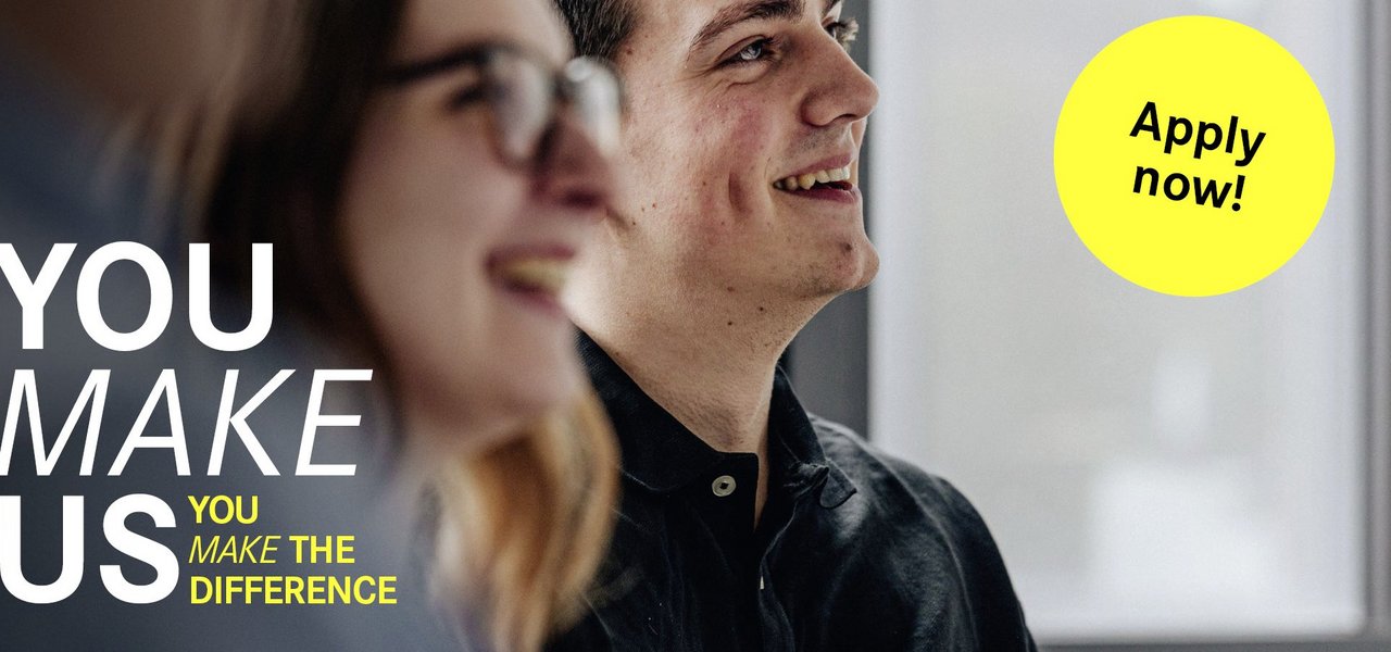 Two young employees during a conversation The slogan "You make us. You make the difference" can be seen on the left-hand side, accompanied by a yellow button with "Apply now!"
