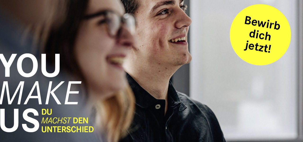Zwei junge Mitarbeitende während eines Gesprächs Der Slogan 'You make us Du machst den Unterschied' ist auf der linken Seite zu sehen, begleitet von einem gelben Button mit 'Bewirb dich jetzt!'