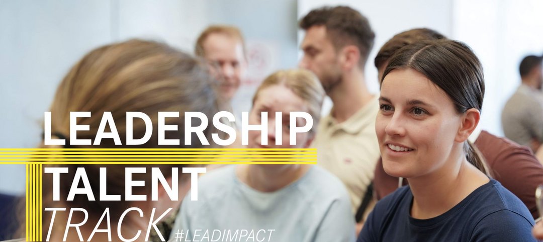 Eine Gruppe junger Daimler Truck Trainees in einer Gesprächssituation. Im Vordergrund ist eine aufmerksam zuhörende Frau und die Schriftzüge „Leadership Talent Track“ und „#LEADIMPACT“.