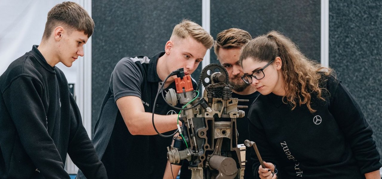 A group of young team members analyse a mechanical device in a workshop.