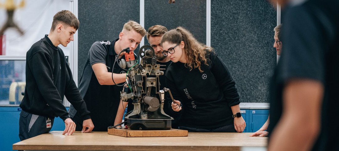 A group of young team members analyse a mechanical device in a workshop.