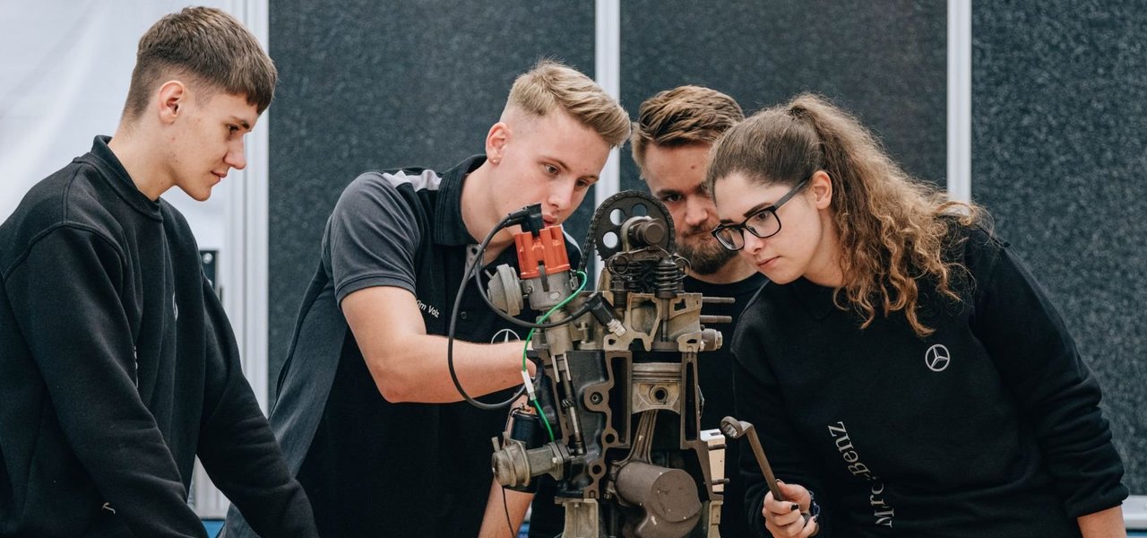 Eine Gruppe von jungen Teammitgliedern analysiert eine mechanische Vorrichtung in einer Werkstatt.