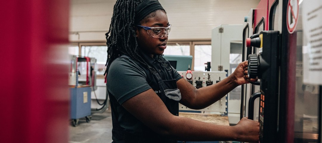 An employee in work clothes and safety goggles concentrates on operating a machine in a factory hall.
