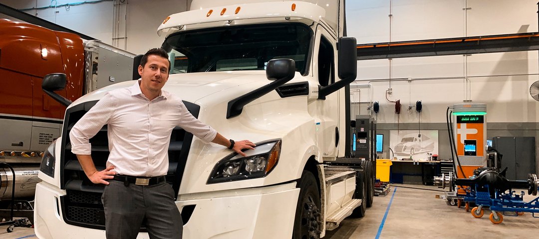 Alexander Voets leans against a white Freightliner eCascadia in a factory hall.