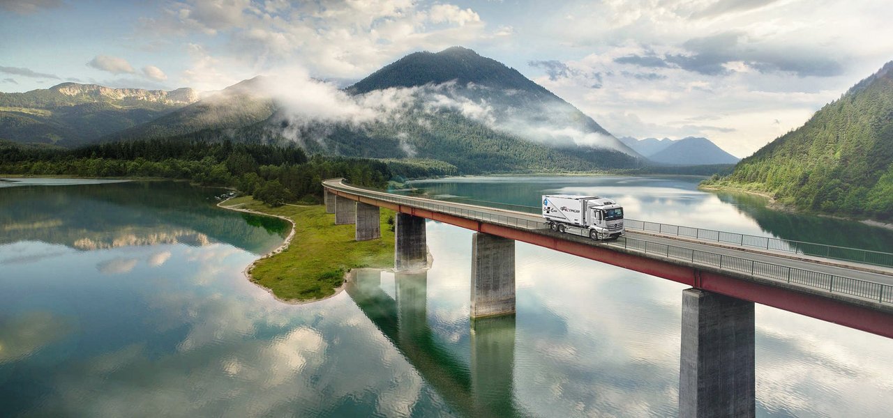 Mercedes-Benz eActros drives over a bridge over a lake in the mountains