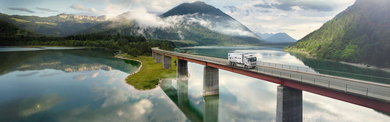 Mercedes-Benz eActros drives over a bridge over a lake in the mountains