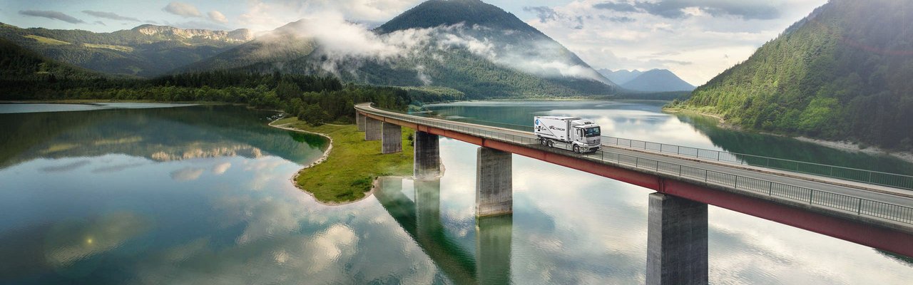 Mercedes-Benz eActros fährt über eine Brücke über einem See in den Bergen